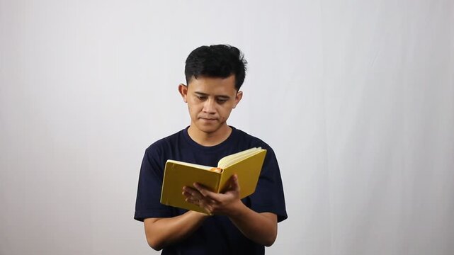 Young man intently reading book, absorbing knowledge and turning pages in simple studio setup