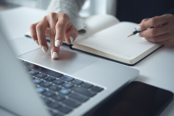 Business woman using laptop computer to search the information and taking note on notebook on...