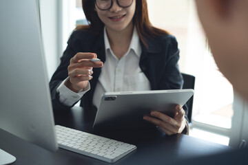 Businessman having a discussion with colleague, working together in office. Two asian business people using digital tablet at meeting. teamwork and collaboration