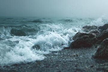 Waves crash against rocky shore at dawn with mist rising from the ocean under a cloudy sky