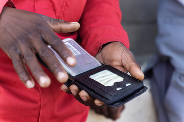 single african worker, opening his wallet counting, credit card and id in docked window, red workwear