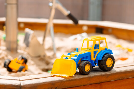 A toy tractor is sitting on a wooden platform in a sandbox
