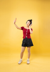 Woman taking a selfie with headphones in casual summer outfit against a yellow background