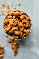 Top view of spicy roasted cashew nuts in a cup on a baking sheet background.
