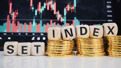 Stacked coins and wooden blocks spelling SET INDEX are in front of stock market chart, symbolizing financial growth and investment