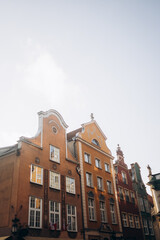 A low-angle view of the colorful, gabled facades of historic townhouses in Gdansk, Poland. The buildings are brightly lit by the sun, set against a clear sky.
