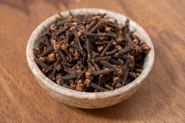 Stone bowl with dried clove buds, used for cooking and traditional medicine, close-up, spices collection