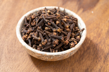 Stone bowl with dried clove buds, used for cooking and traditional medicine, close-up, spices collection