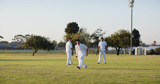 Raising bat Indian male batsman swinging bat on pitch, male fielder retrieving ball hurling back