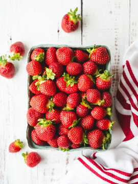 Carton of fresh strawberries on white wood backdrop from above.