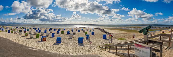 Fast menschenleerer Strand von Utersum auf der Nordseeinsel F&ouml;hr mit Strandk&ouml;rben, und der von leichter Bew&ouml;lkung verdeckten Sonne im Gegenlicht