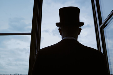 Back view of middle aged man wearing top hat standing near open window looking outside at cloudy sky, silhouette emphasizing formal attire and contemplative posture
