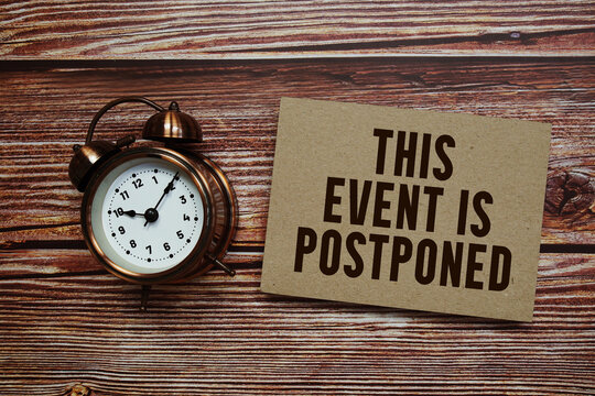 This event is postponed text with alarm clock on wooden background