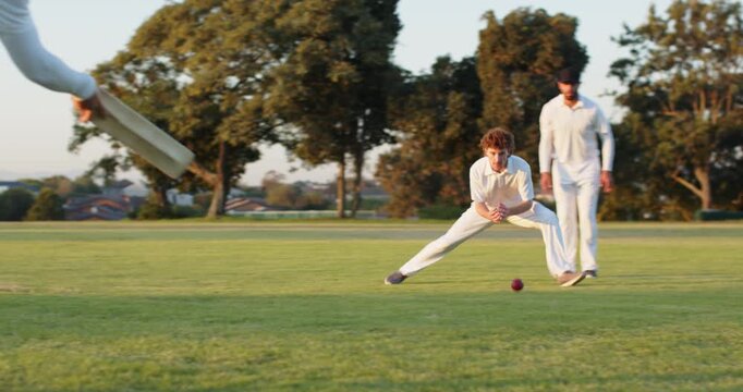 During practice male teammates swinging shot and diving catch cricket ball on outfield copy space