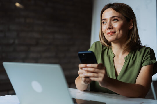 Casual business woman using phone while working in modern office - Powered by Adobe
