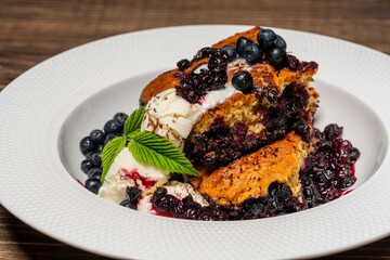 White plate with piece of fresh baked blueberry cobbler and ice cream on wooden background, closeup. Homemade berry cobbler ready to eat