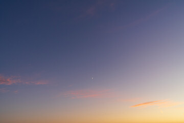 Serene twilight sky with a beautiful color gradient from orange to blue, featuring a waxing crescent moon and clouds.