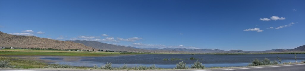Panoramic view of a serene lake bordered by distant mountains under a clear blue sky