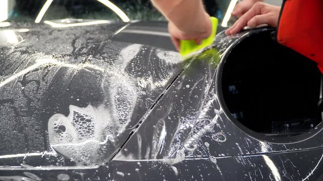 A car wrapping specialist applies a polyurethane film to the car. Detailer smoothes PPF. Car wrapping, detailing, tuning and styling. PPF protective film against chips and scratches. Car protection.
