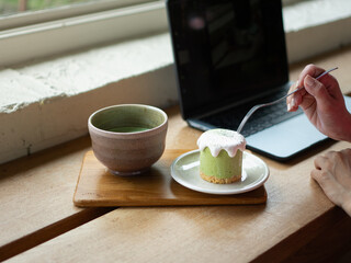 Working at cafe, A matcha mousse cake with cream topping, served on a small plate and wooden tray in warm tones