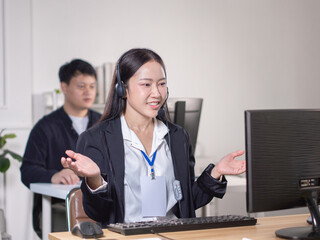 Fototapeta premium An Asian woman in a suit and a headset is explaining in front of a computer, similar to a call center.