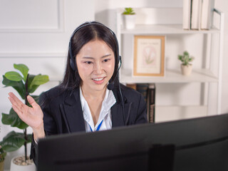 An Asian woman in a suit and a headset is explaining in front of a computer, similar to a call center.