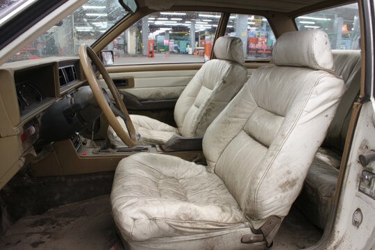 Fototapeta Interior of a vintage car.  Cream-colored, worn leather seats. Dusty interior.  Steering wheel, dashboard visible