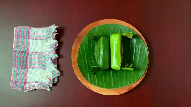 4K overhead view hand placing wooden plate with lemper on banana leaf. Warm sticky rice and savory chicken scent, perfect for culinary, tradition, and celebration themes.