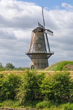 The impressive "De Hoop" windmill on a dike in Gorinchem, Netherlands, stands tall on an earthen rampart, under a bright, cloudy Dutch sky.