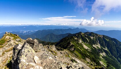 Fototapeta premium Panoramic view of a mountain range, showing rocky foreground and lush green slopes receding into distant blue mountains under a partly cloudy sky