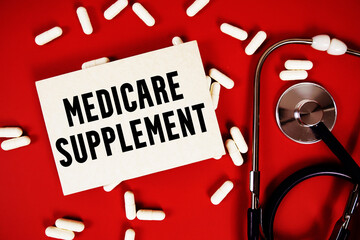 Medicare Supplement text written on paper card with stethoscope and medicine capsule on red background