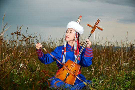 Mongolian female musicians in traditional Mongolian attire playing the morin khuur on the grasslands