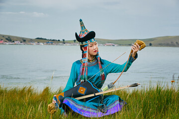 Mongolian girls dressed in traditional Mongolian attire and holding bows and arrows by a lake on...