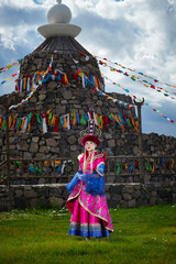 Naklejka premium Mongolian girls dressed in luxurious Mongolian costumes in front of an obo on the grassland