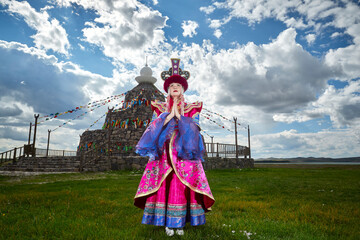 Mongolian girls dressed in luxurious Mongolian costumes in front of an obo on the grassland