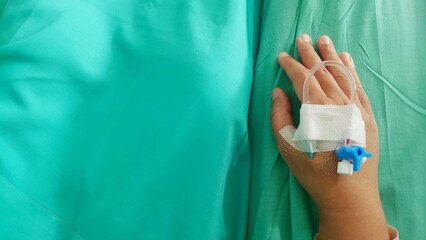 Fototapeta premium Close-up of a hand with an IV drip attached, lying on a hospital bed with a green sheet and patient wristband visible.