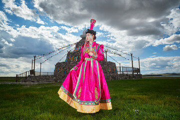 Mongolian girls dressed in luxurious Mongolian costumes in front of an obo on the grassland