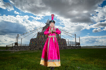 Mongolian girls dressed in luxurious Mongolian costumes in front of an obo on the grassland