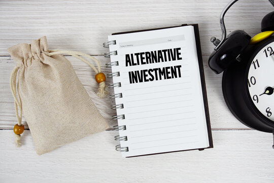 Alternative Investment text with money bag and alarm clock on wooden background