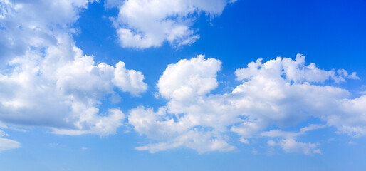 Gentle white cumulus clouds gently drift across a clear blue daytime sky. This is a calm and peaceful view of the sky, suggesting fair weather conditions