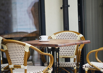 Outdoor cafe table with wicker chairs and white cup on the table.