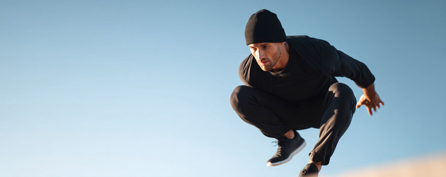 Athletic man leaping against a clear sky. Symbolizes ambition, freedom, and overcoming challenges. Great for fitness, lifestyle, and motivational content. Inspiring.