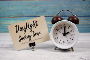 Daylight Saving Time  text written on paper card with alarm clock on wooden background