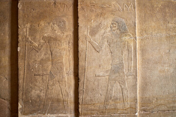 Low relief image of the tomb of Ty showeing two standing men with staffs and scepters  under hieroglyphic text from the mastaba of the Old Kingdom, Saqqara,