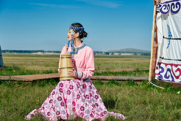 Fototapeta premium A Mongolian girl wearing Mongolian attire and holding a bucket of milk tea in front of a yurt.