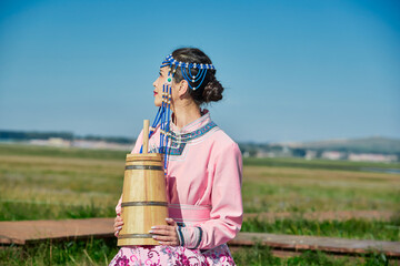 A Mongolian girl wearing Mongolian attire and holding a bucket of milk tea in front of a yurt.