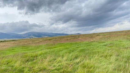 Obraz premium Vast grassy field under a cloudy sky with distant mountains