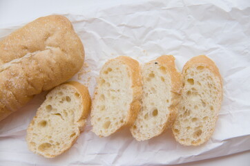 Freshly baked and sliced baguette on a crinkled white paper, highlighting its delicious crust and soft interior.
