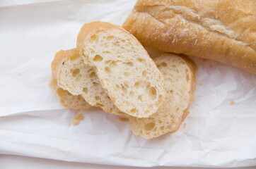 Freshly baked and sliced baguette on a crinkled white paper, highlighting its delicious crust and soft interior.