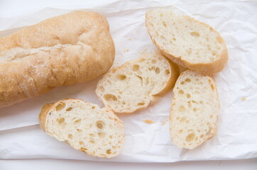 Freshly baked and sliced baguette on a crinkled white paper, highlighting its delicious crust and soft interior.